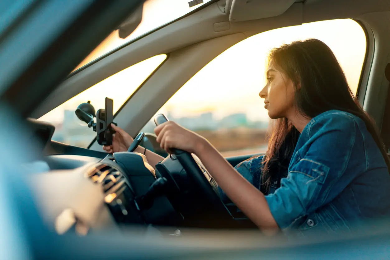 woman in car driving and looking at phone